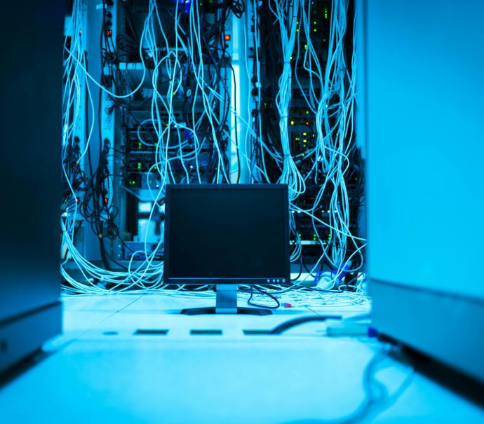 A complex network of cables in a data center with a monitor in the foreground.